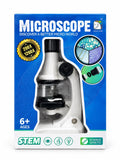 A boxed toy or educational microscope set on a plain white background. The retail package is blue with large white 'MICROSCOPE' text, a photo of a white and black microscope through a clear window, and feature callouts including '200X 1200X', '6+ AGES', 'STEM', and 'SCIENCE GENETIC'.